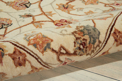 Beige floral area rug with cream background, brown border, and multicolor leaf motifs on a light wood floor.