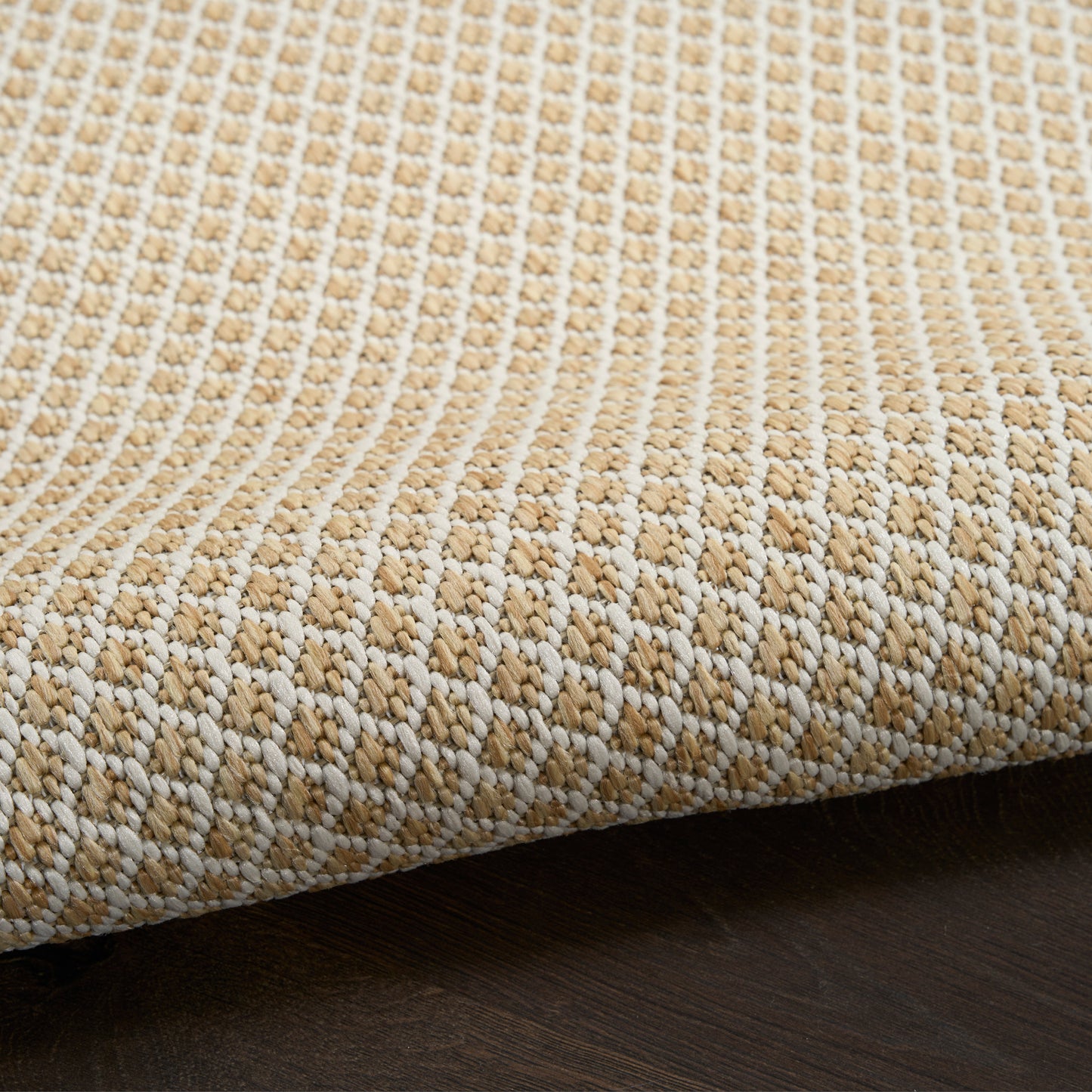 Beige and white woven round rug with a chunky textured checkerboard pattern on dark wood floor.