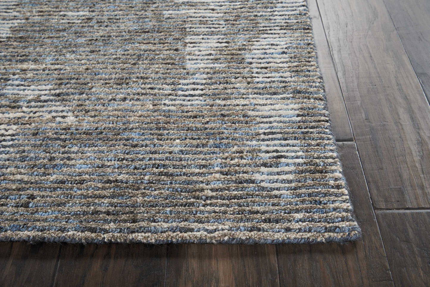 Textured striped area rug in blue, beige and gray hues on dark wood floor.