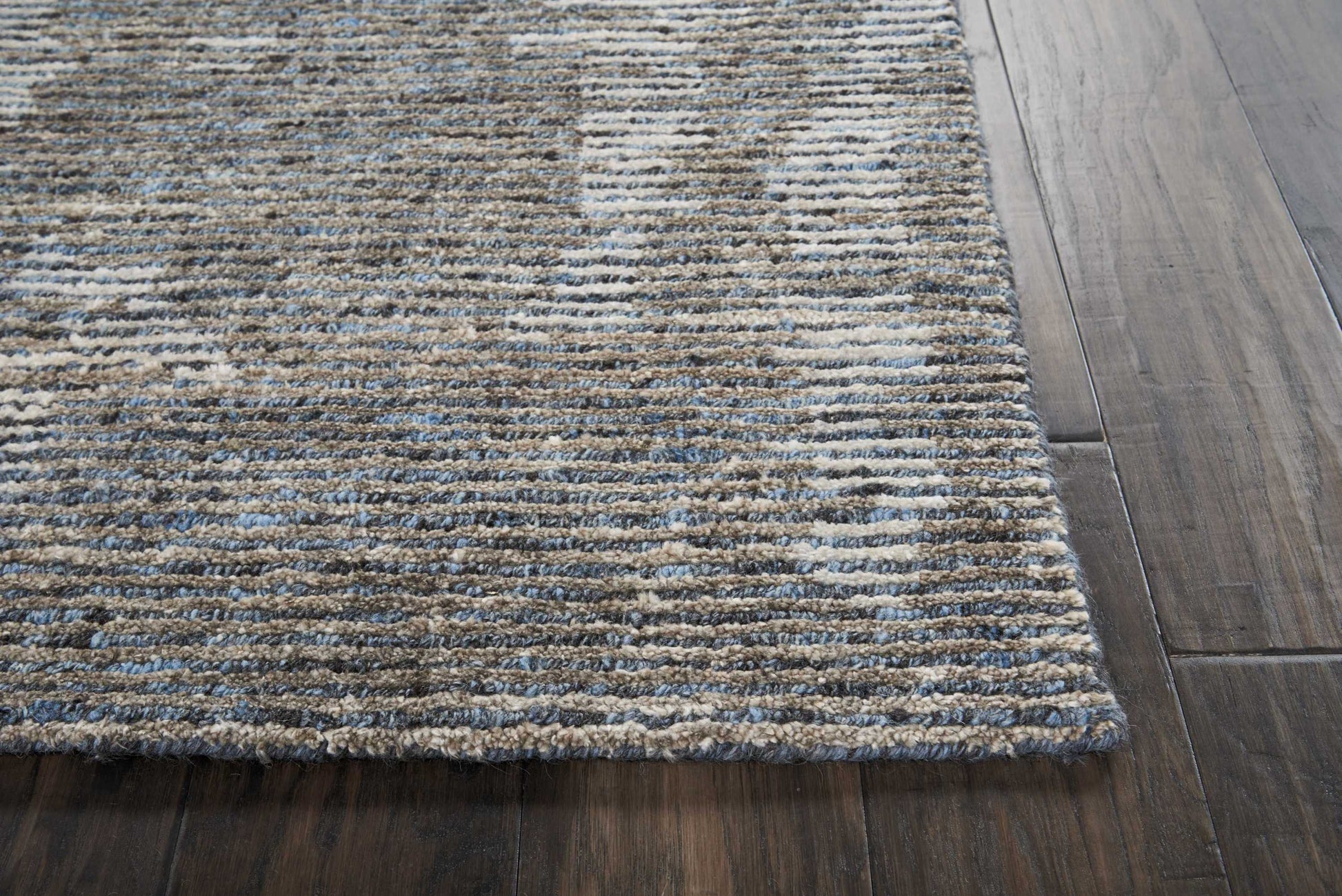 Textured striped area rug in blue, beige and gray hues on dark wood floor.