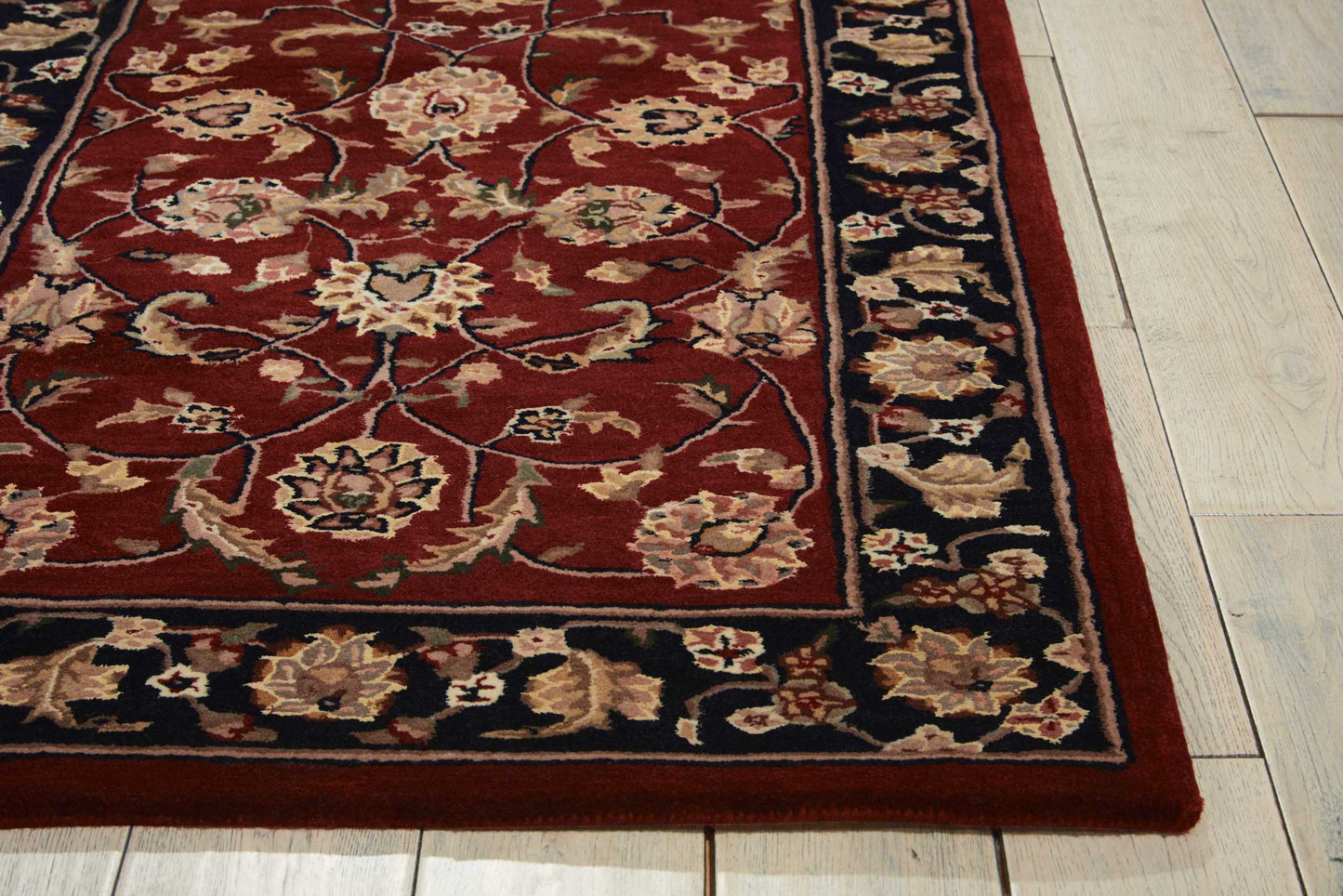 Red oriental rug with intricate floral pattern and a navy border with beige flowers on a light wooden floor.