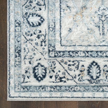 Cream rug with blue ornate border and medallion design on dark wood floor.