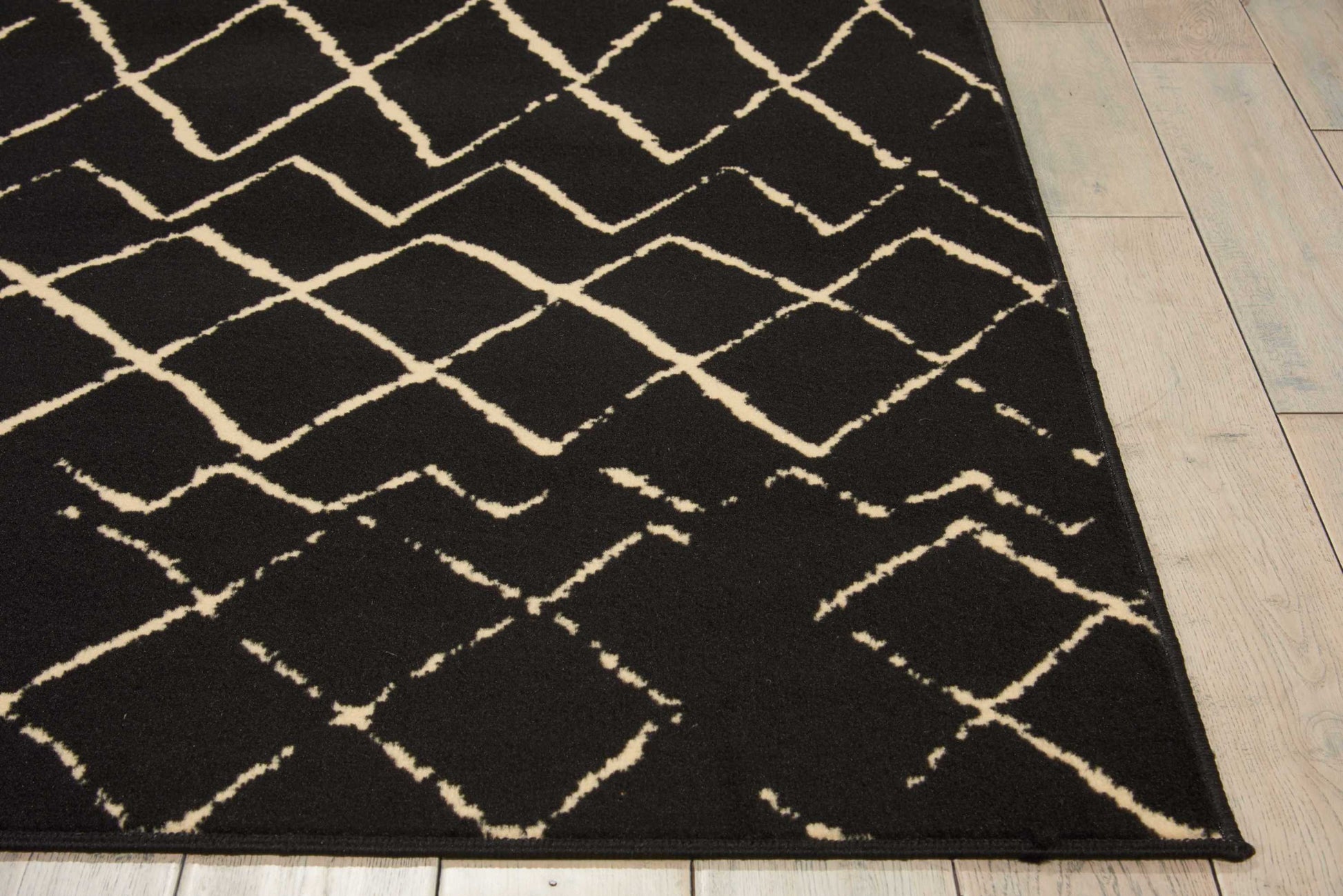Black area rug with cream diamond lattice pattern, modern geometric style on light wood floor.