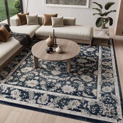 Round wooden coffee table on a blue and cream ornate rug, beige sectional with tan and taupe pillows, plant nearby.
