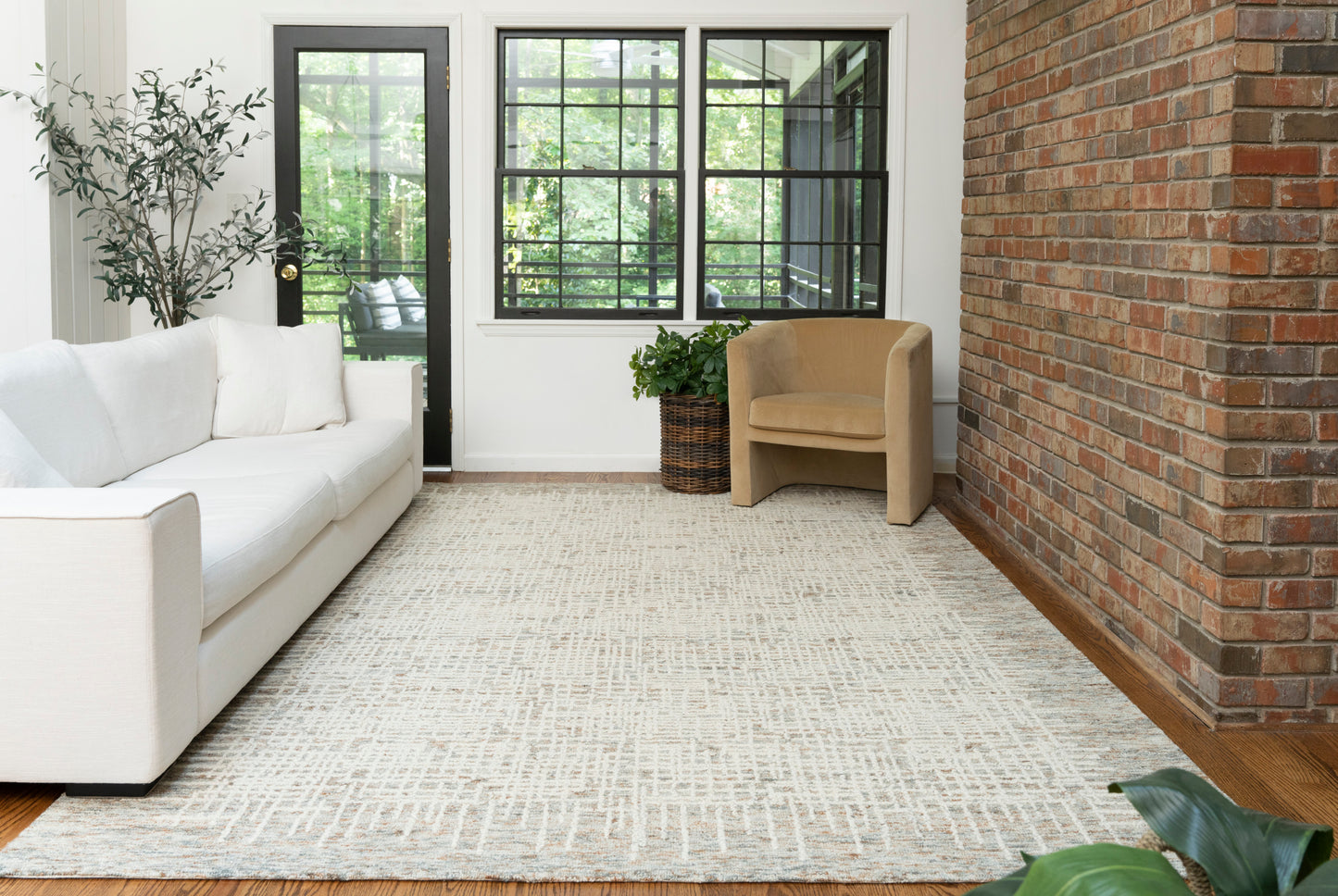 Light beige textured area rug with subtle geometric pattern under white sofa and tan armchair in a bright living room.