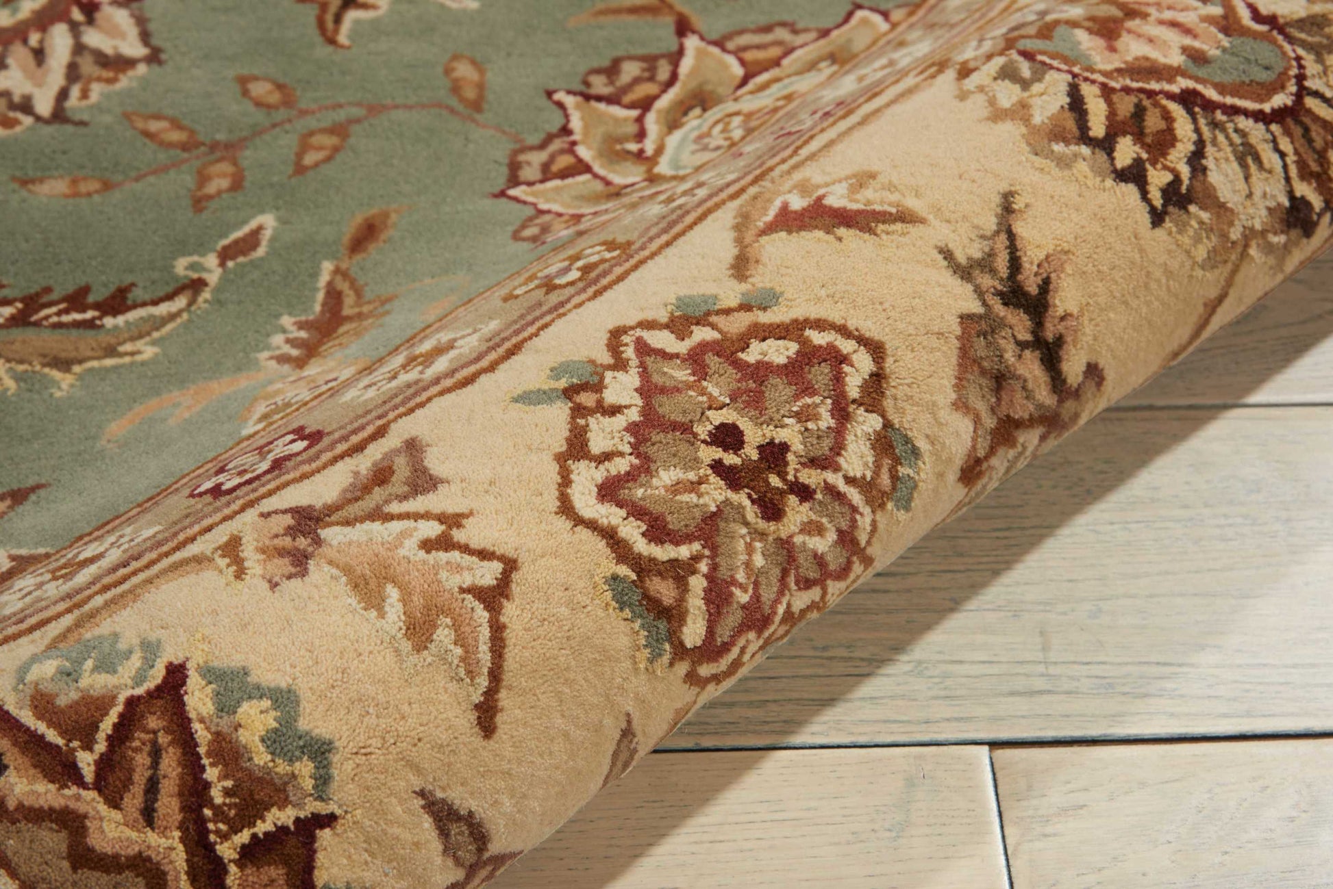 Beige ornate floral rug rolled up, teal and red accents, on light wood floor.