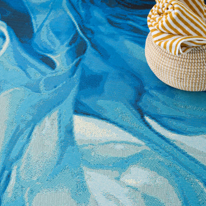 Blue textured rug with a woven straw sunhat resting on a yellow-and-white striped towel.