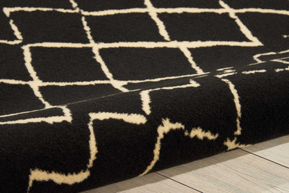 Black plush rug with cream geometric grid pattern, folded edge resting on light wooden floor.
