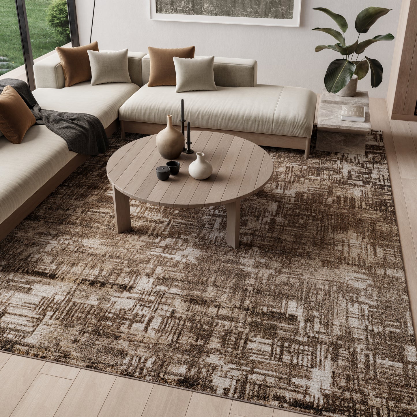 Neutral beige sectional sofa with tan & beige cushions, round wood coffee table, ceramic vases & candles, brown geometric rug, potted plant.