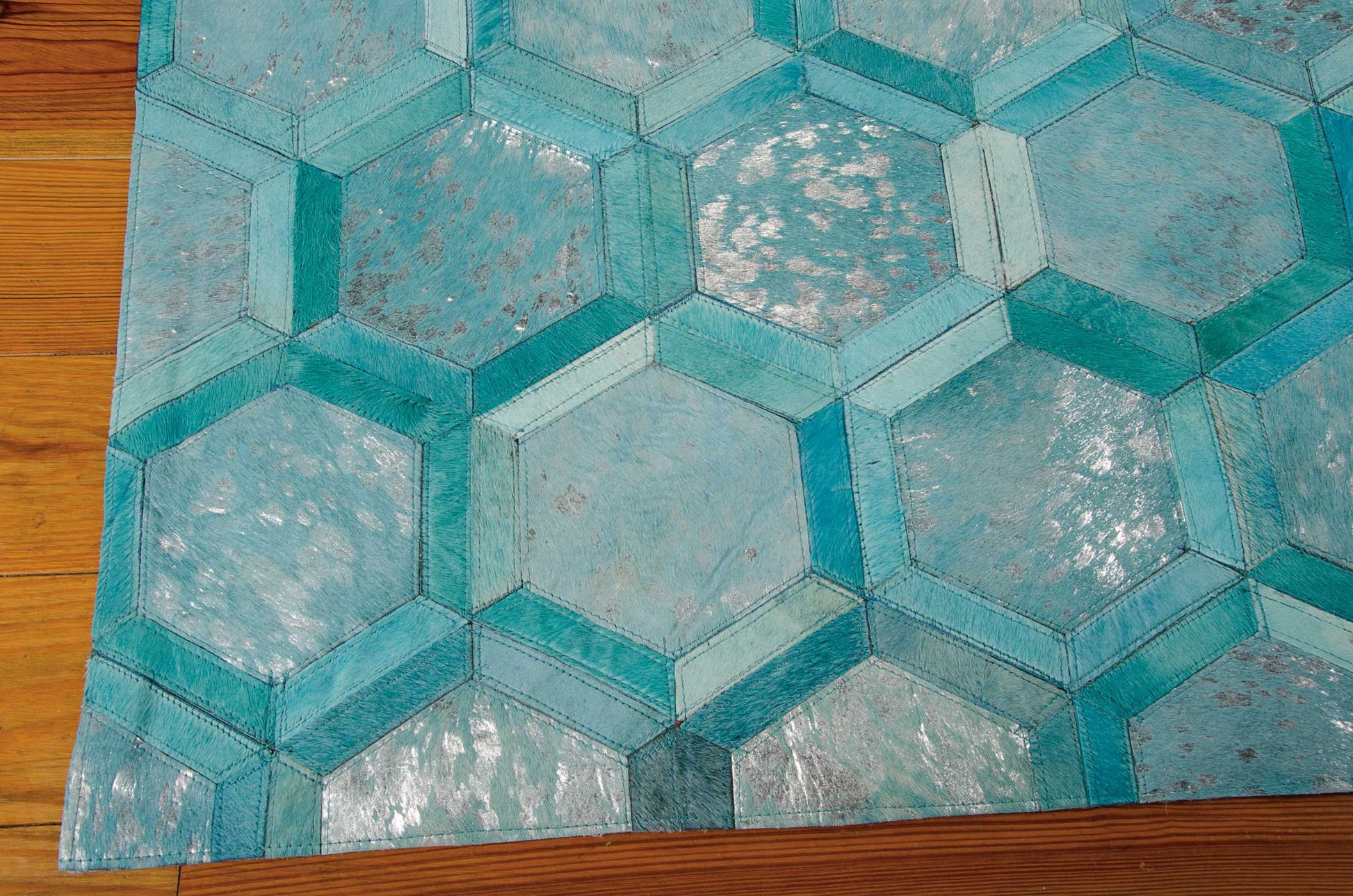 Teal and turquoise hexagon-pattern rug with stitched geometric tiles in blue shades on a wooden floor.