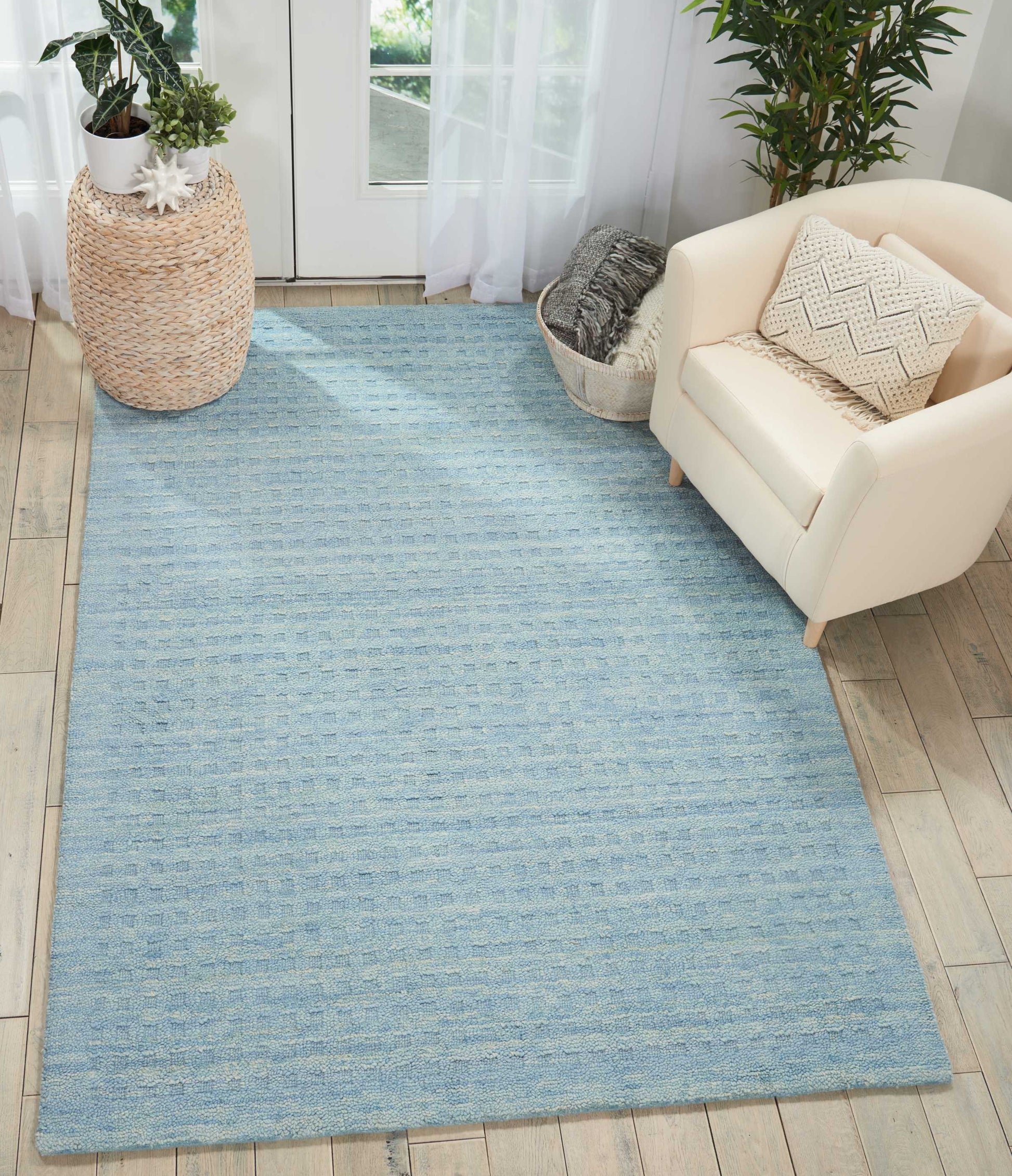 Light blue rectangular woven area rug on light wood floor, with a cream armchair and natural woven baskets.