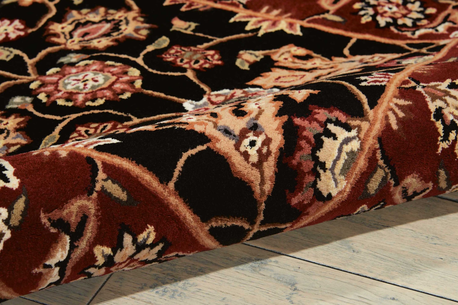 Close-up of a red oriental rug with cream floral pattern on a dark background, on a light wooden floor.