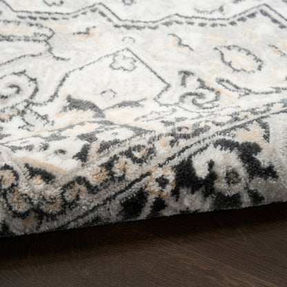 Soft plush area rug with cream base, gray and black Persian-inspired border, tan accents on dark wood floor.