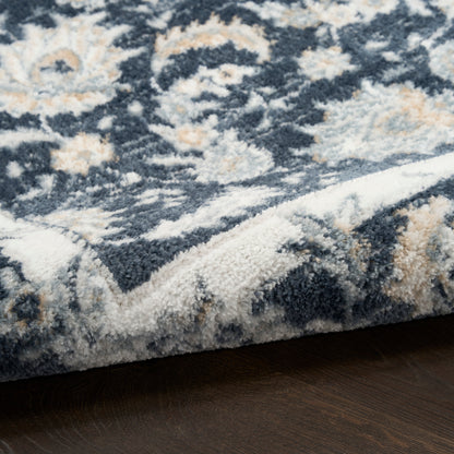 Plush blue-gray Persian-style rug with ivory and beige floral motifs; rolled edge on dark wood floor