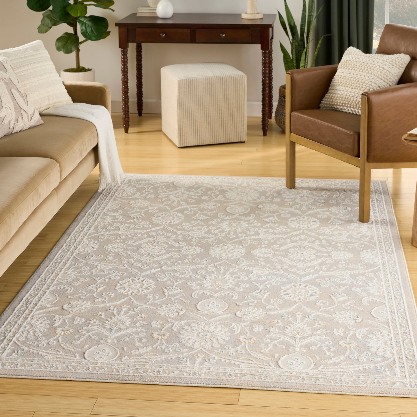 Beige damask area rug in cream and gray on light wood floor, styled with tan sofa and brown leather chair.