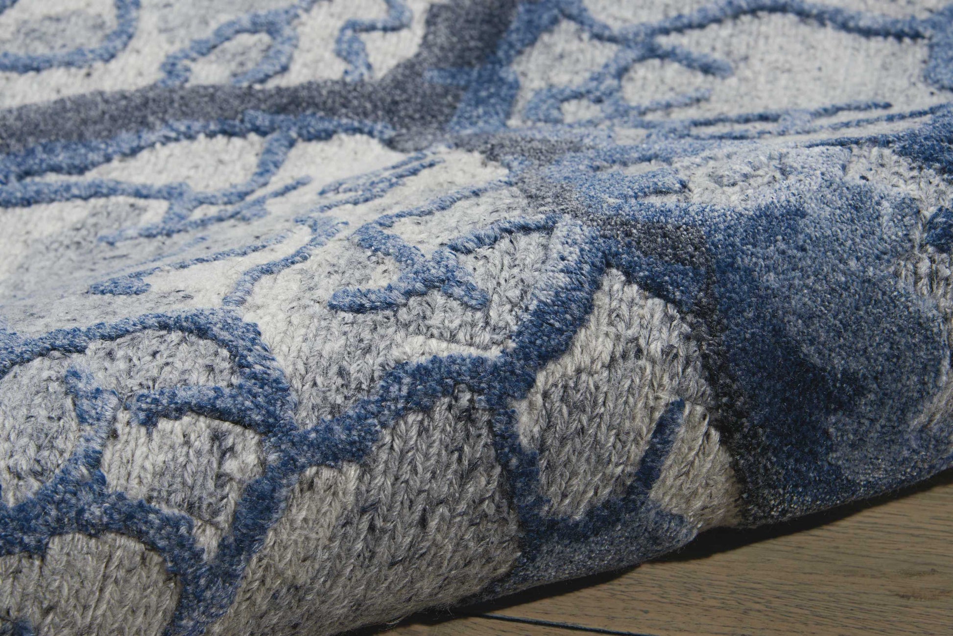 Close-up of blue and gray geometric area rug with plush pile, edge detail, on wooden floor.