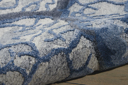 Close-up of blue and gray geometric area rug with plush pile, edge detail, on wooden floor.