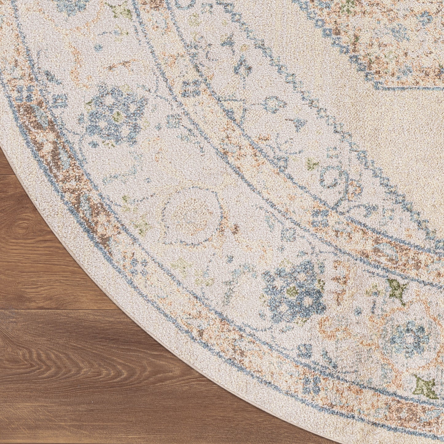Round ivory rug with distressed blue and tan floral medallion pattern on wood floor.