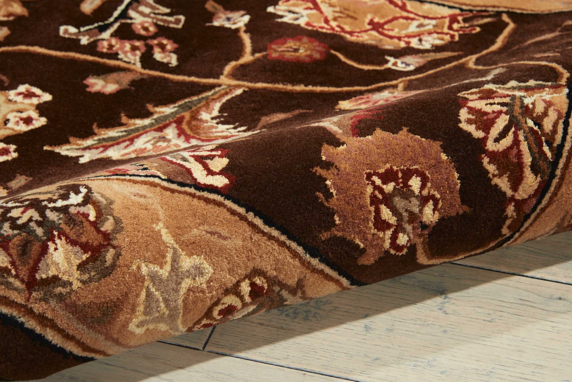 Brown oriental rug with beige, cream & red floral motifs, thick pile, folded on a wooden floor.