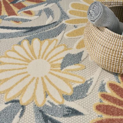 Woven floral area rug with oversized cream-yellow daisies and blue-grey leaves beside a round rattan basket.