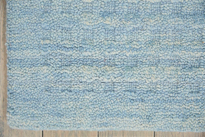 Blue shaggy rug with light to medium blue bands on a wooden floor; soft tufted pile.