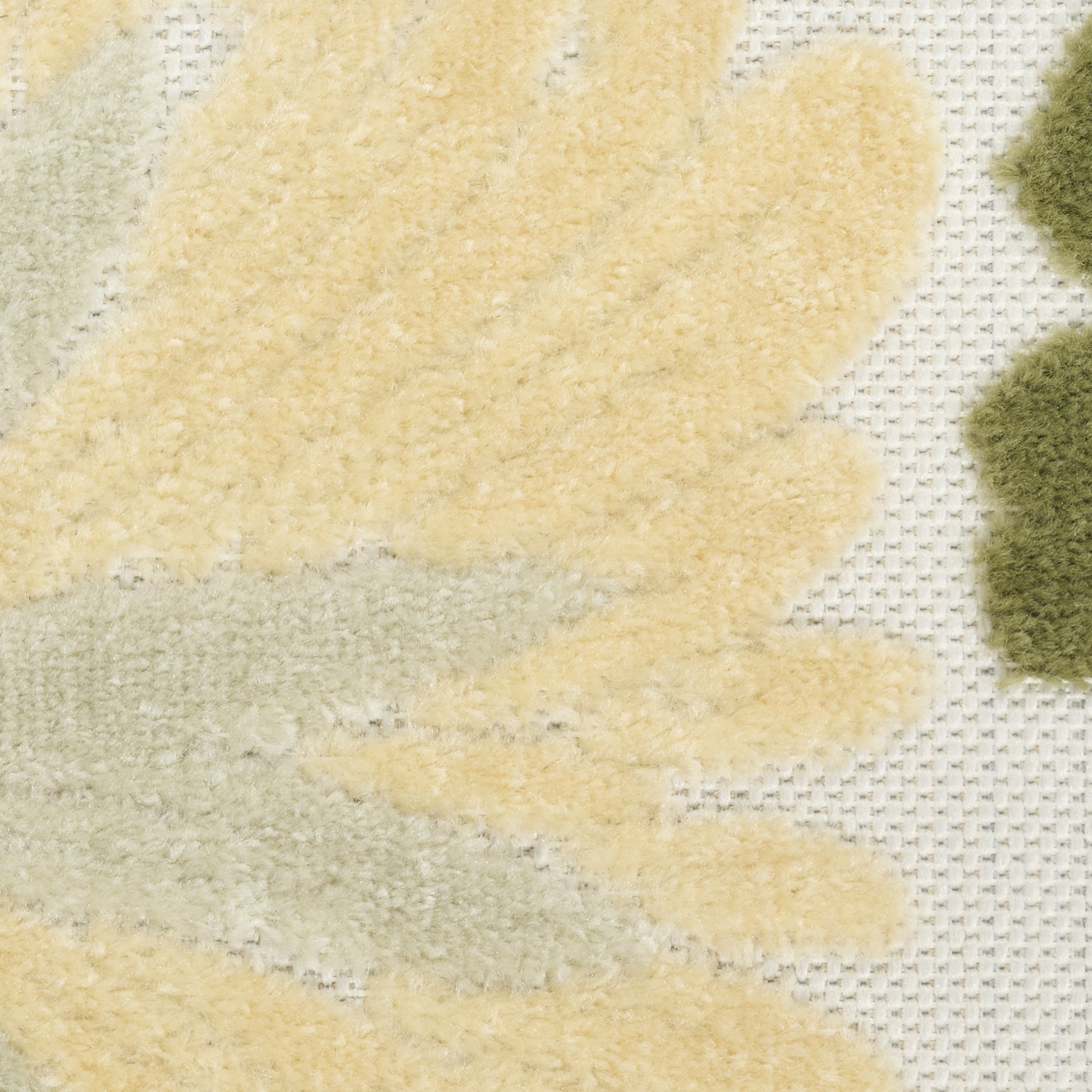 Close-up of a textured rug with pale yellow and light gray leaf shapes on a cream grid background.
