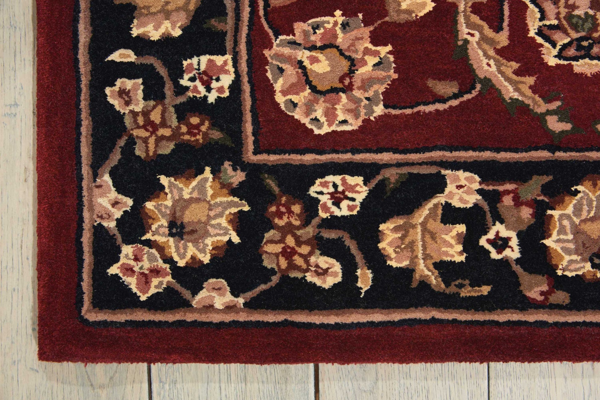 Oriental-style rug with red border and black field, cream and gold floral motifs, on a light wooden floor.