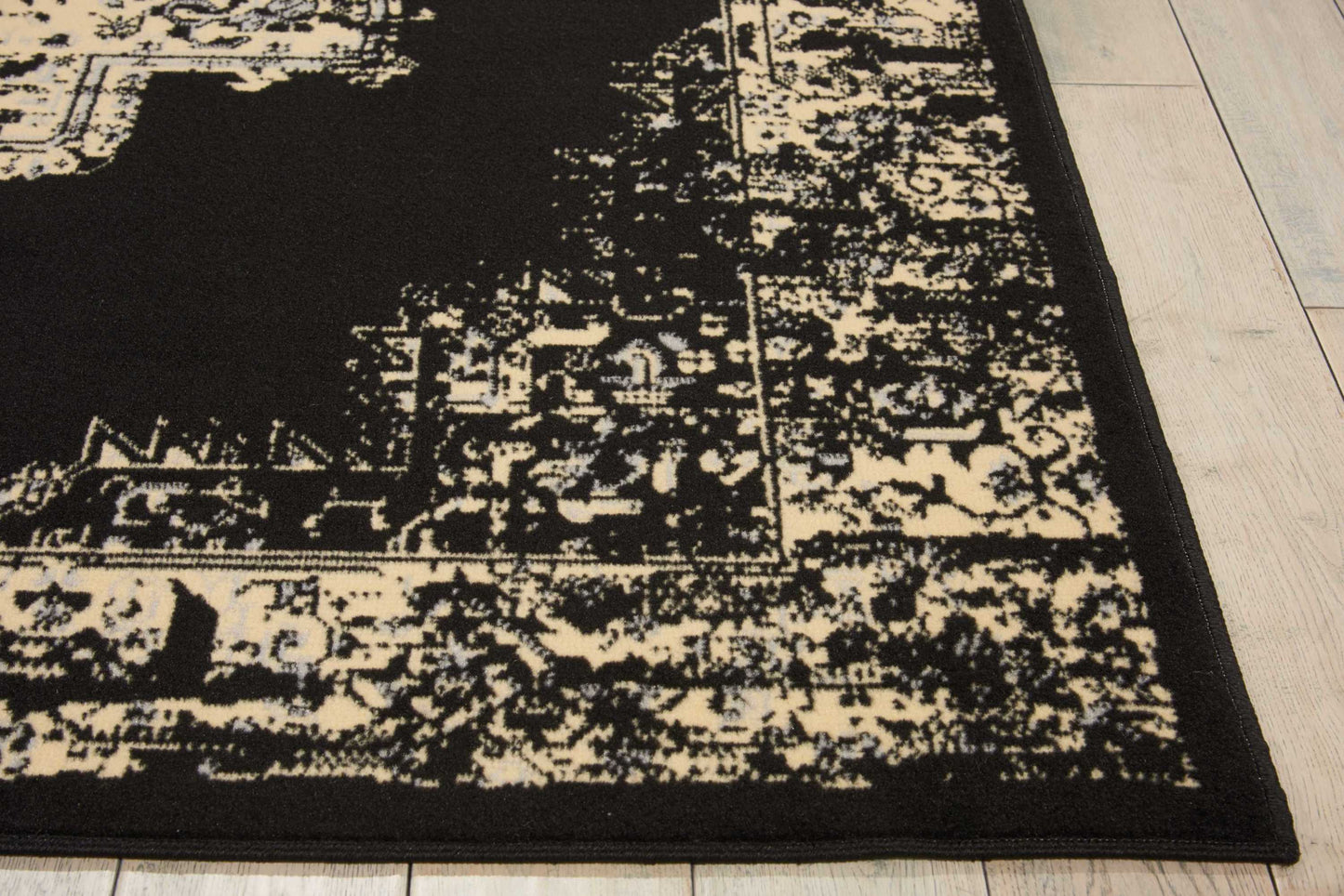 Rectangular black and cream distressed Oriental rug with ornate border, laid on light wood flooring.