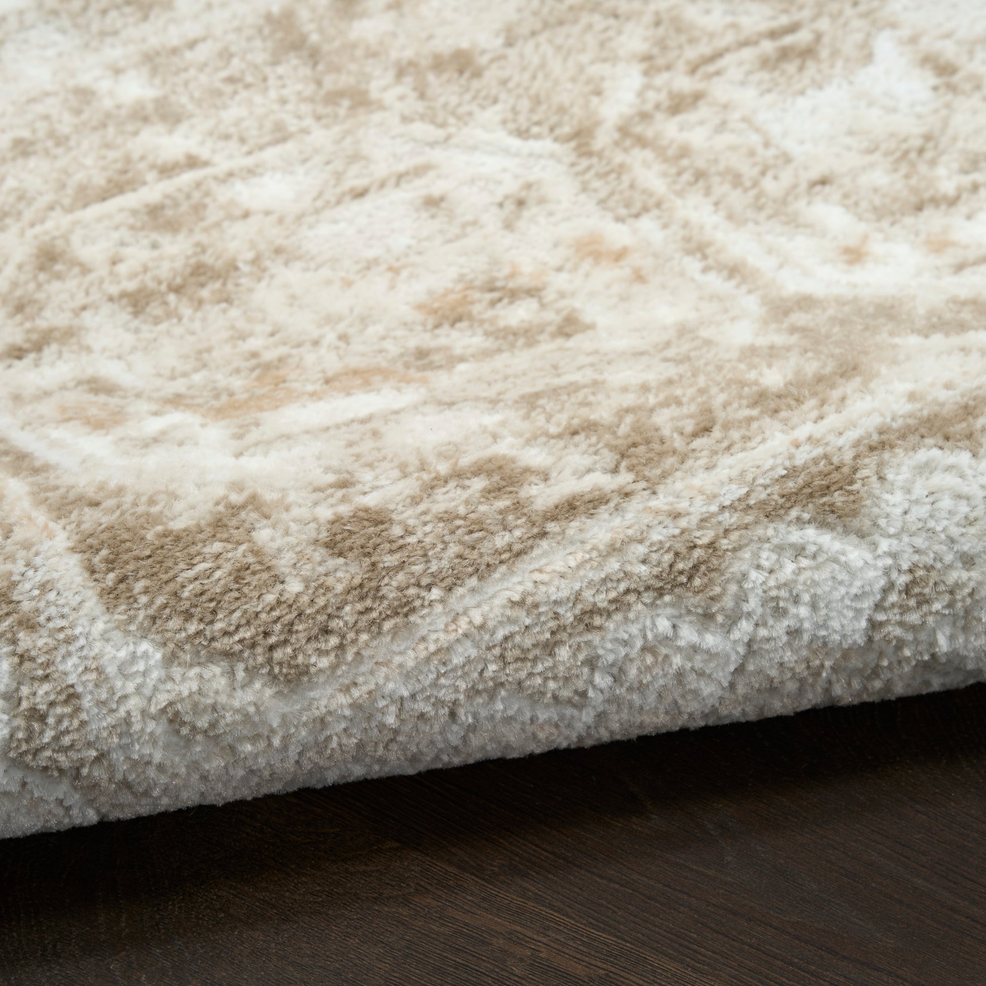 Cream shag rug with thick plush pile and tonal pattern on dark wood floor.