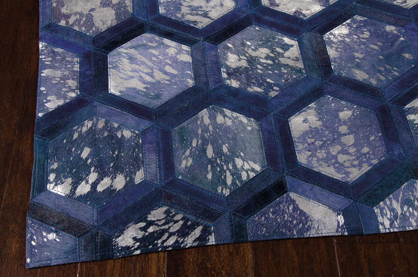 Quilted blue hexagon rug with navy borders and speckled light blue panels on dark hardwood floor.
