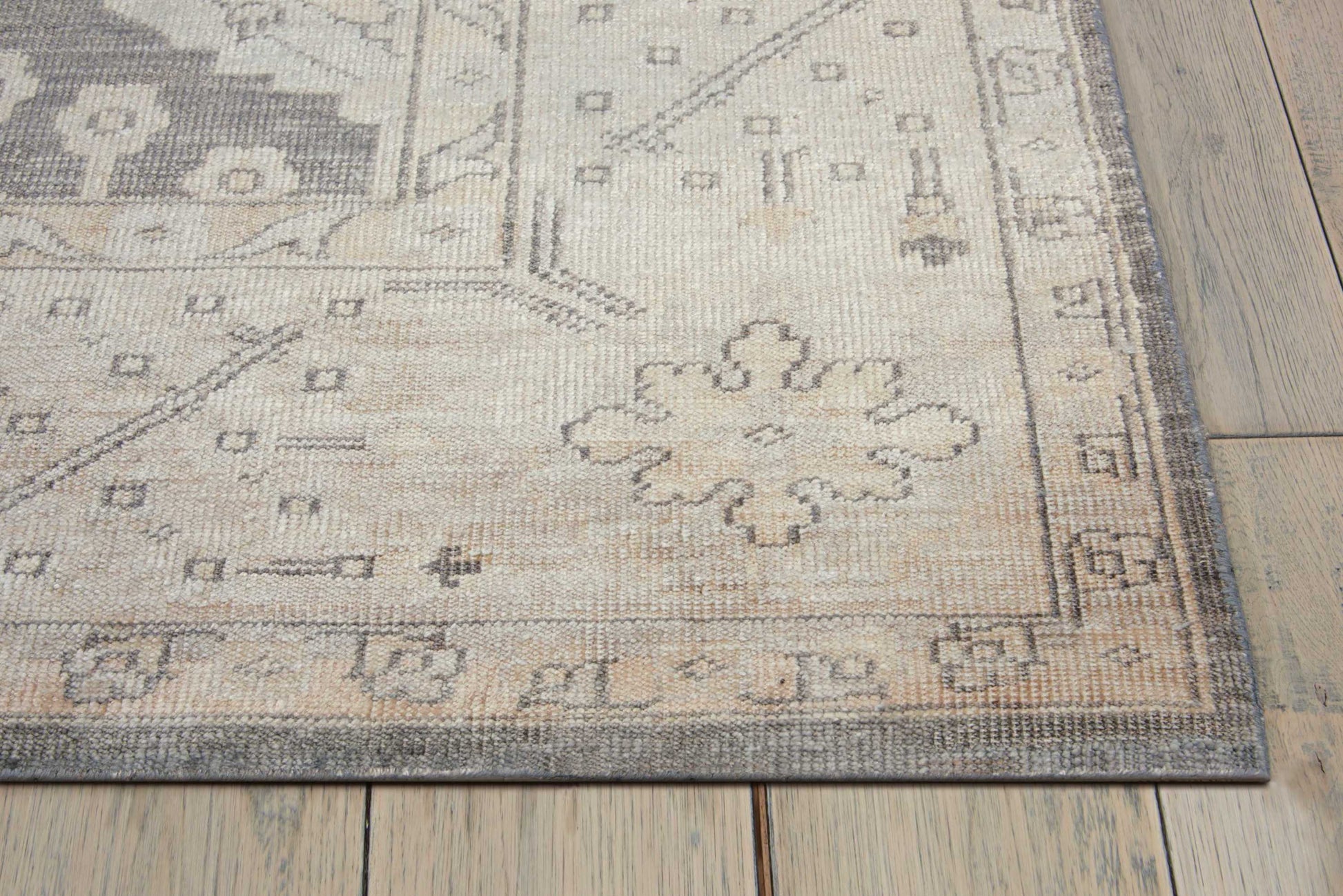 Beige-gray oriental-style area rug with subtle floral medallion pattern and decorative border on wooden floor.