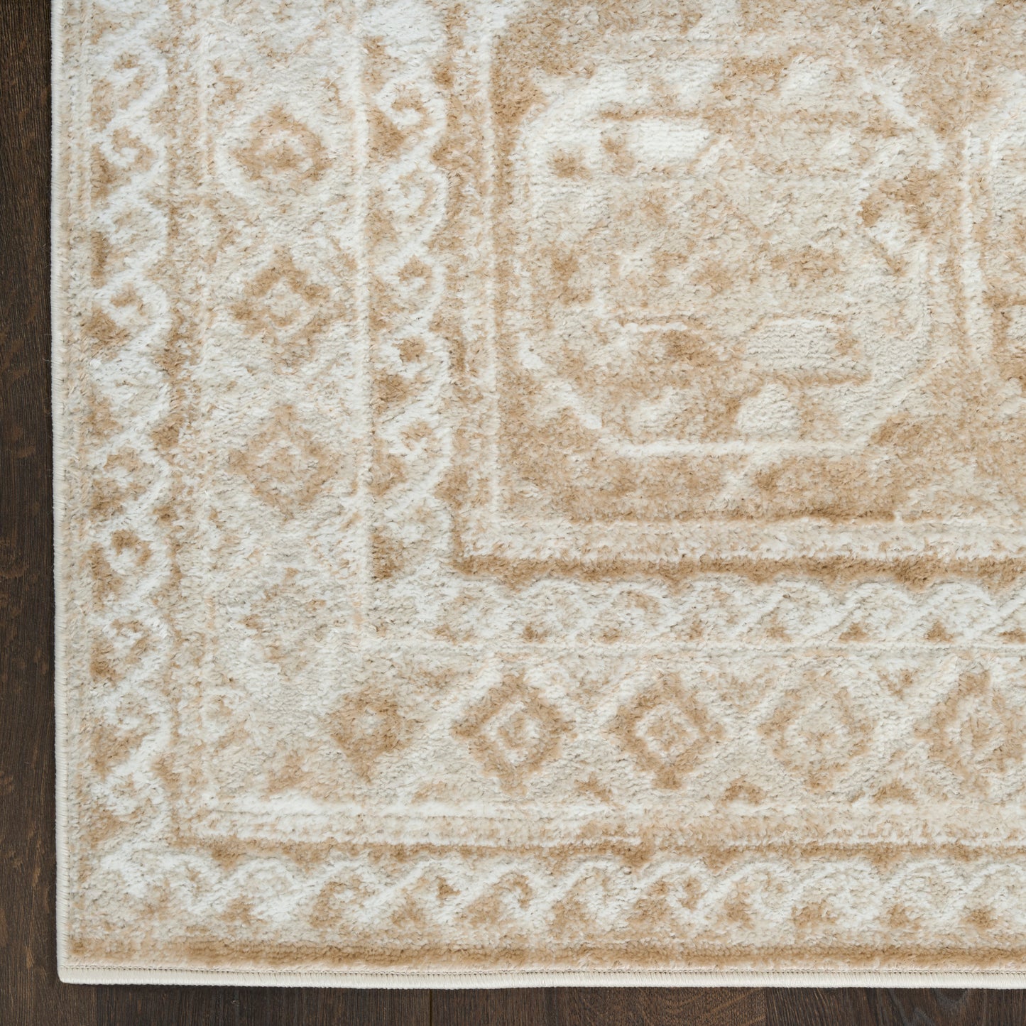 Beige and ivory traditional area rug with medallion center and diamond borders on dark wood floor.