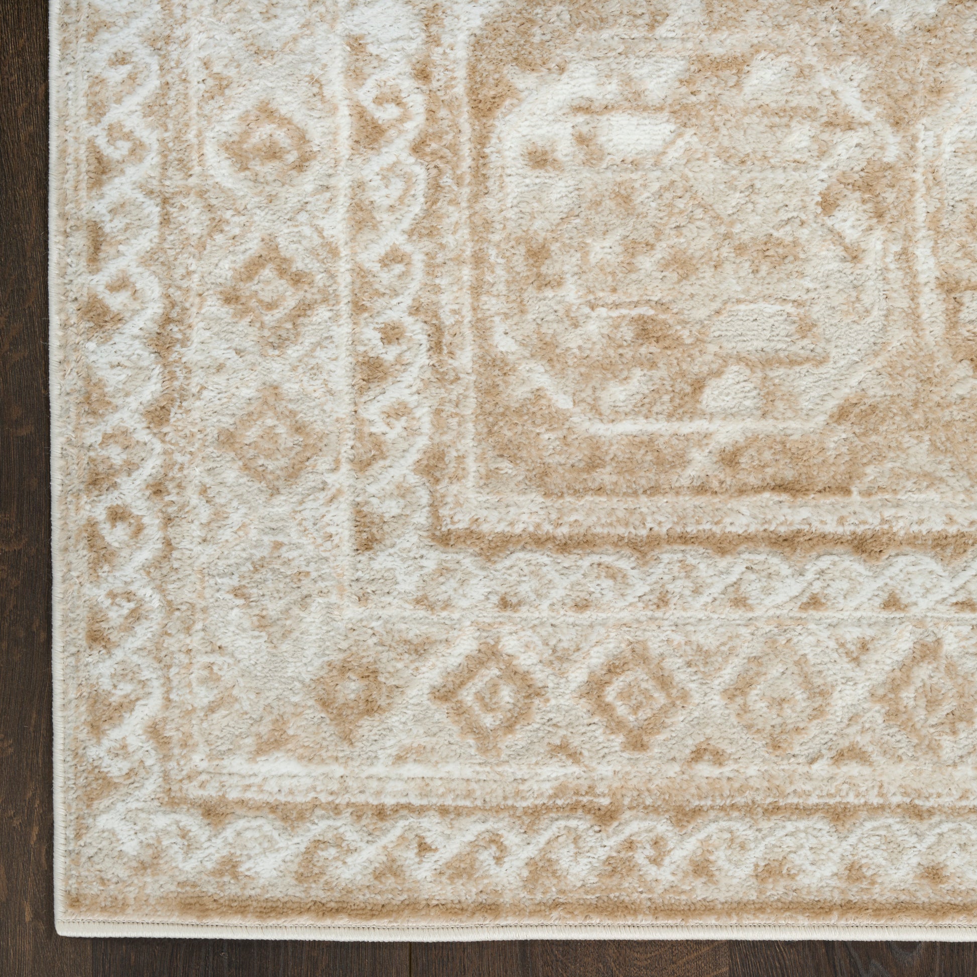 Beige and ivory traditional area rug with medallion center and diamond borders on dark wood floor.