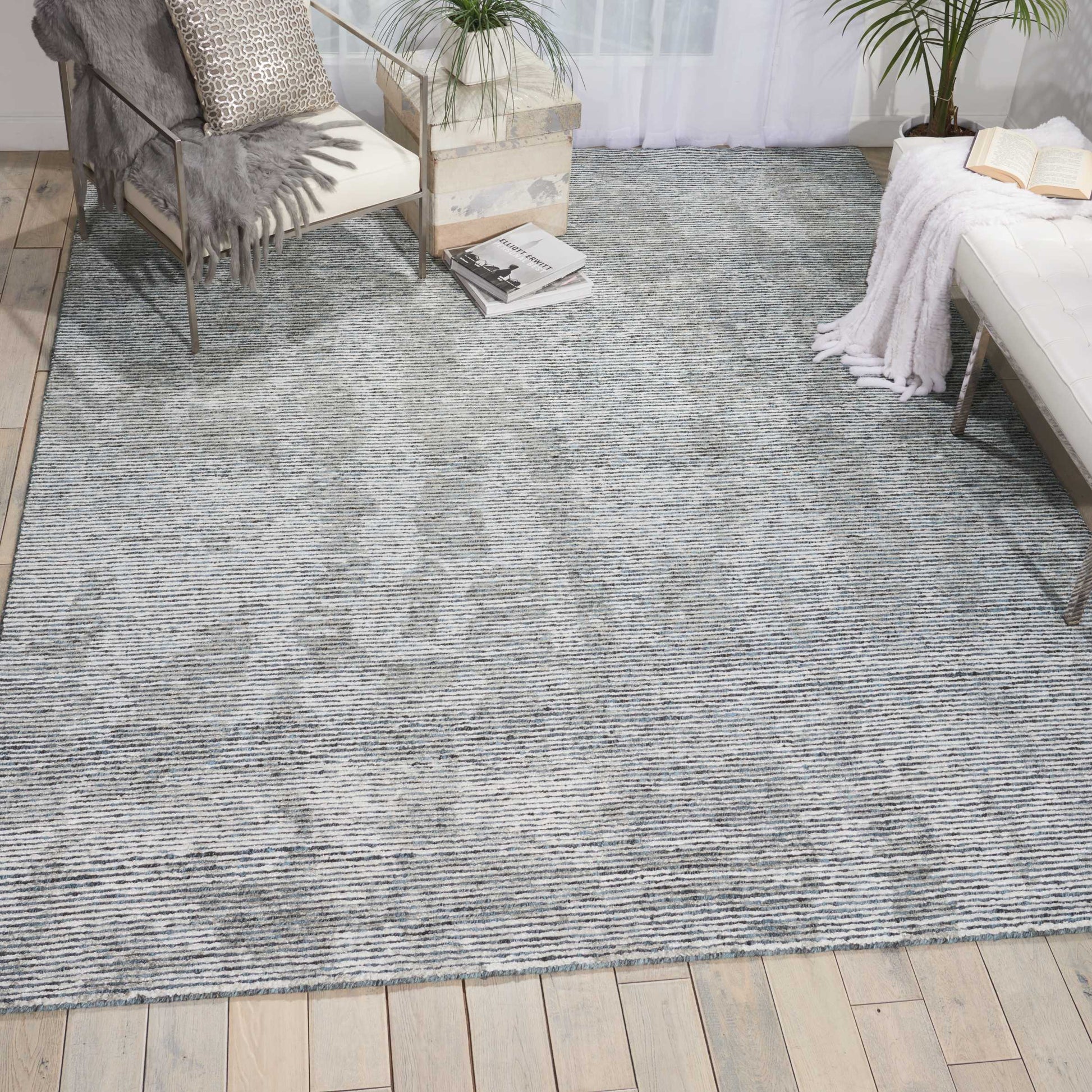 Blue gray woven textured area rug on light wood floor; cozy living room with plants, a metal-framed chair, and a white sofa.