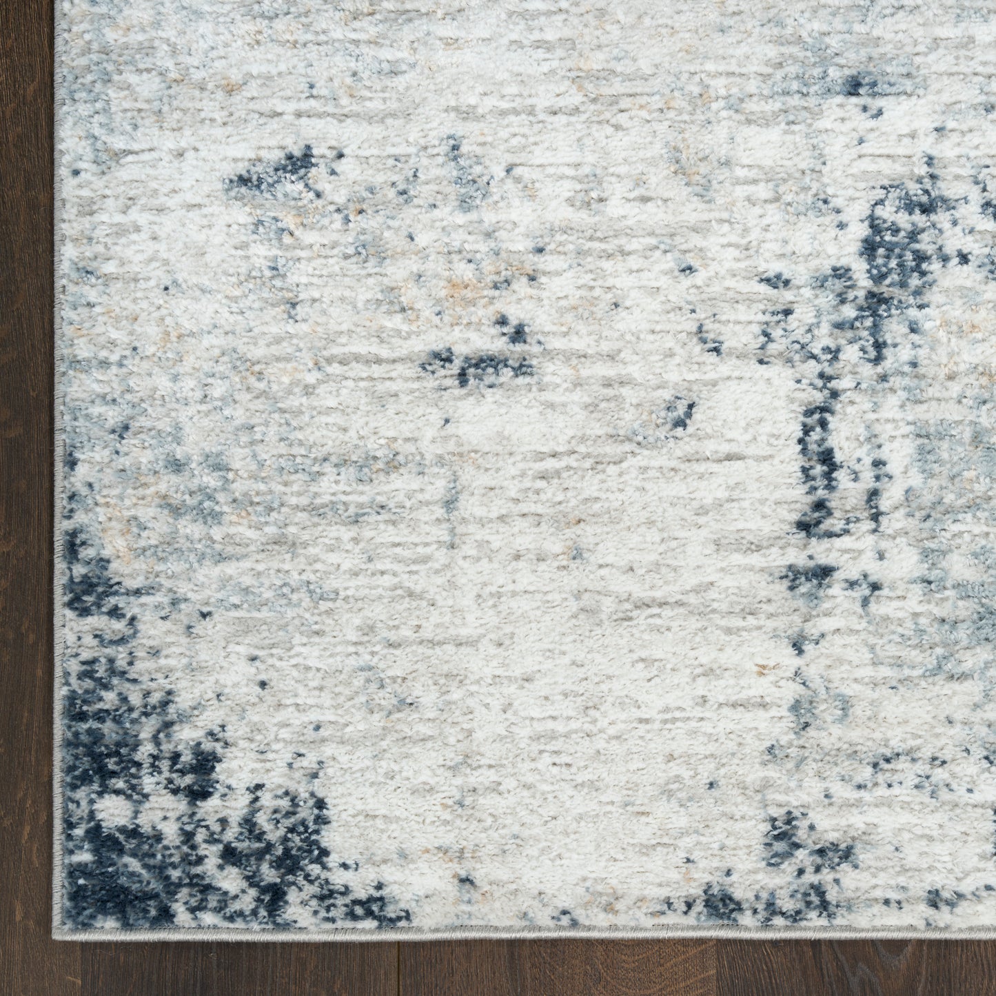 Cream and blue distressed area rug with abstract pattern on dark wood floor.