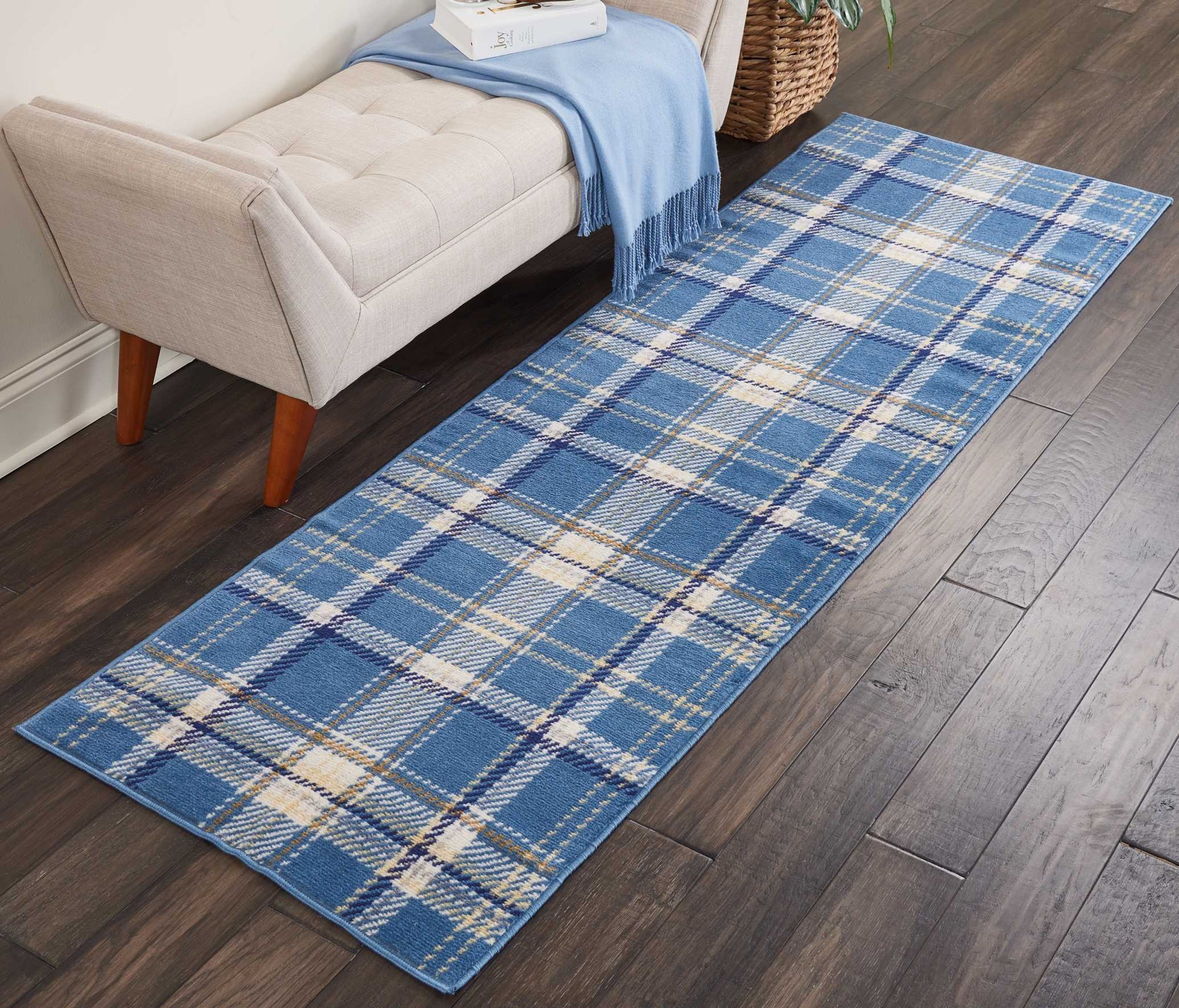 Blue plaid runner rug with cream and navy lines, woven fabric, long narrow rug beside a beige sofa on a dark wood floor.