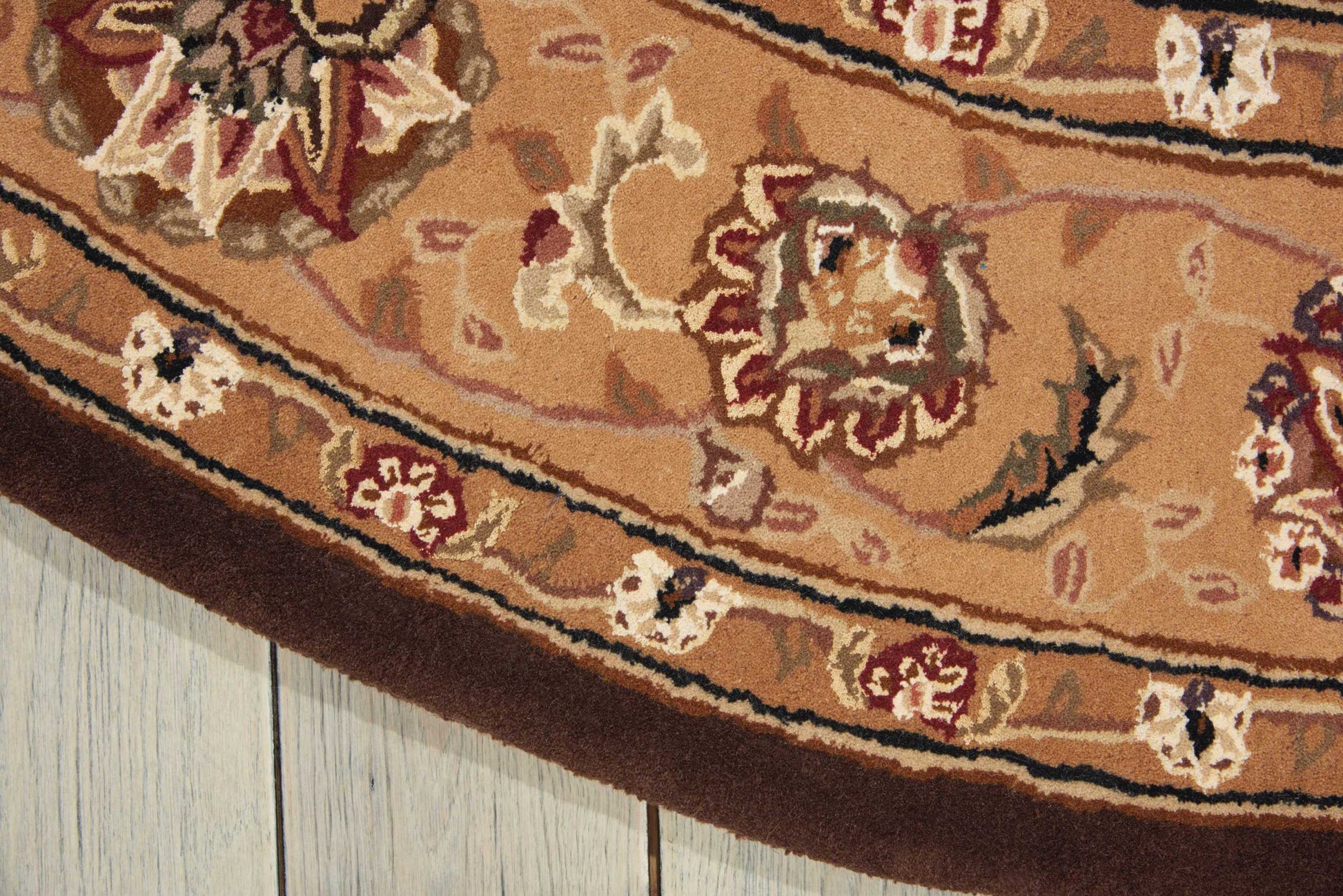 Round oriental rug with tan-brown field, red and ivory floral motifs and decorative border on wooden floor.