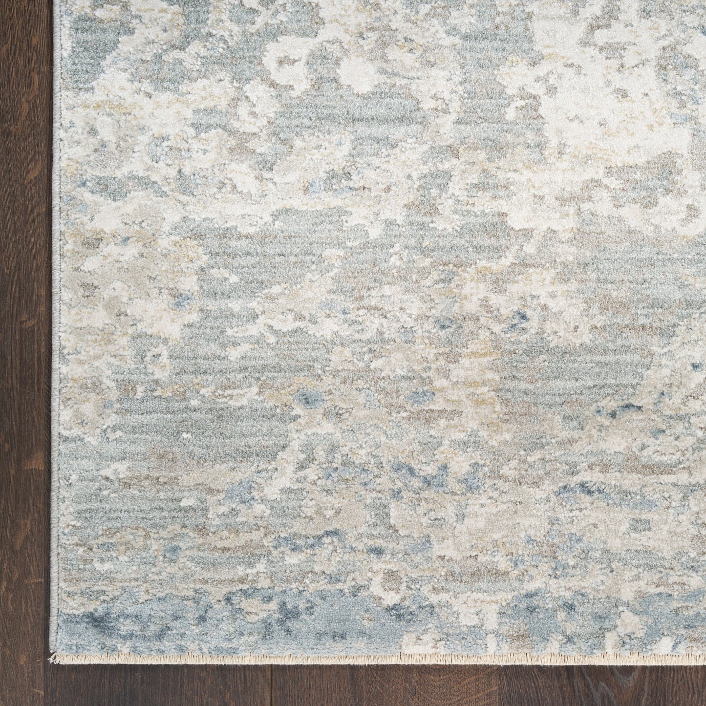 Blue and beige distressed area rug with gray accents in an abstract pattern on dark hardwood floor.
