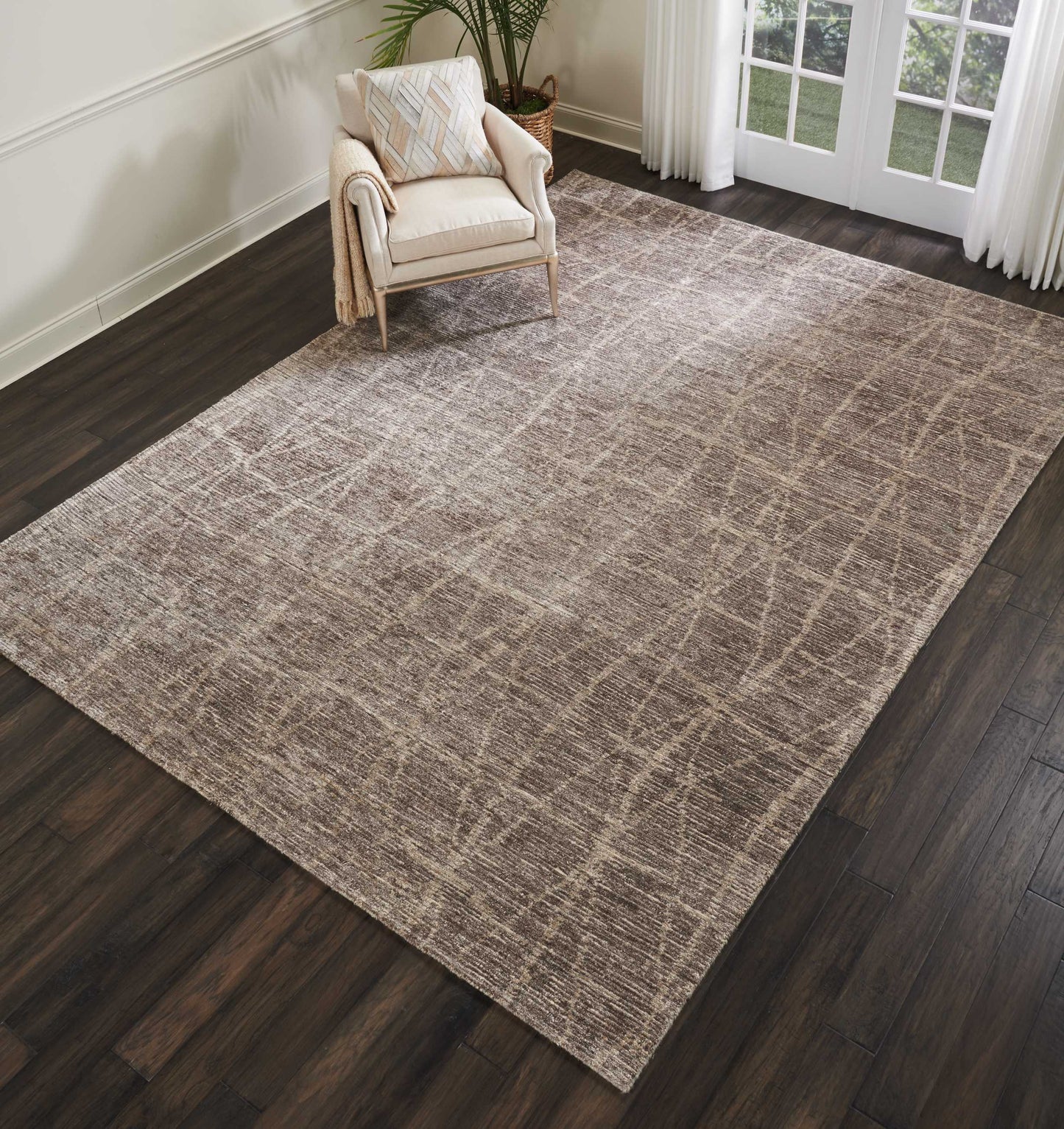 Neutral taupe-gray area rug with subtle crosshatched grid pattern on dark hardwood floor, beige armchair and plant by French doors.