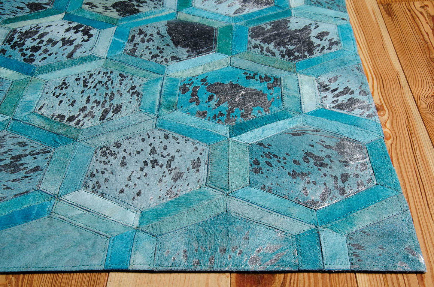 Turquoise hexagon patchwork rug with stitched borders and speckled panels on a wooden floor.