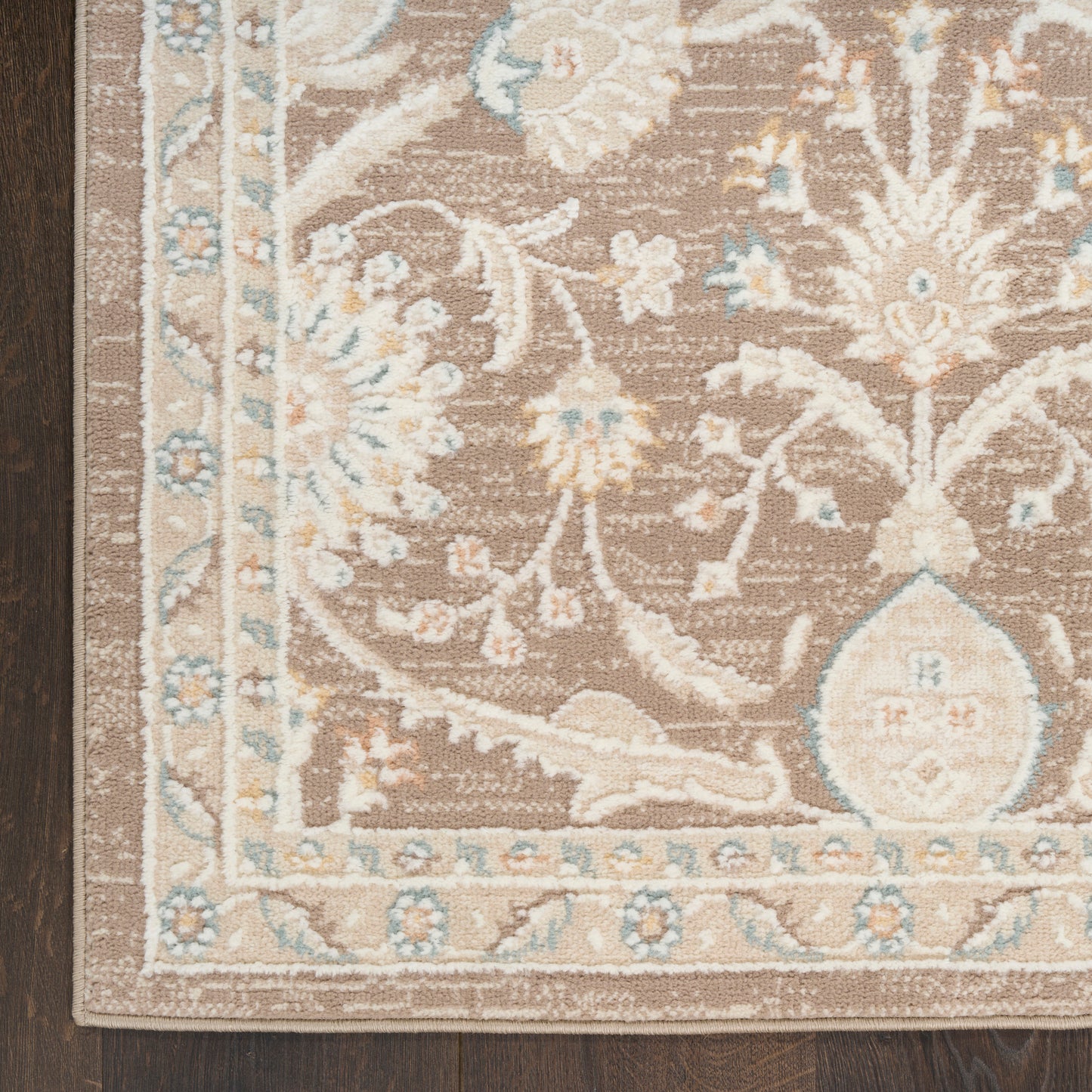 Brown floral patterned area rug with ivory and light blue accents and decorative border on dark wood floor.