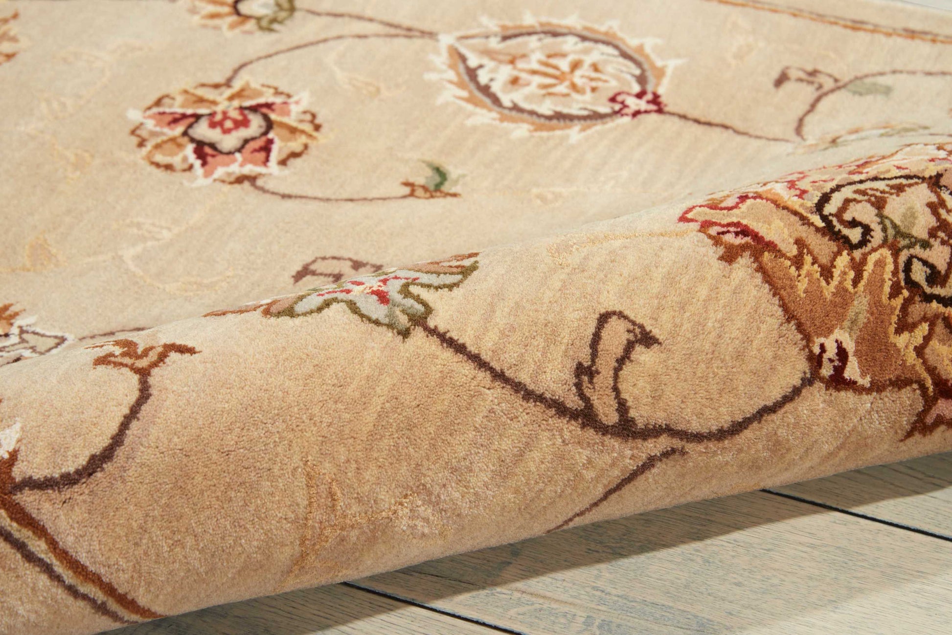Beige oriental rug with brown and red floral motifs, green leaves, thick plush pile on light wood floor.