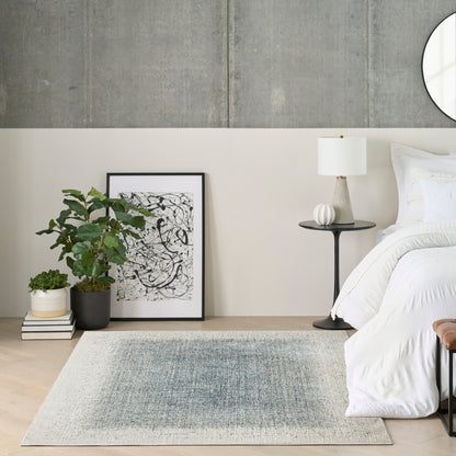 Contemporary bedroom with concrete wall, white bedding, black round side table, lamp, abstract art, plant, books, gray rug.