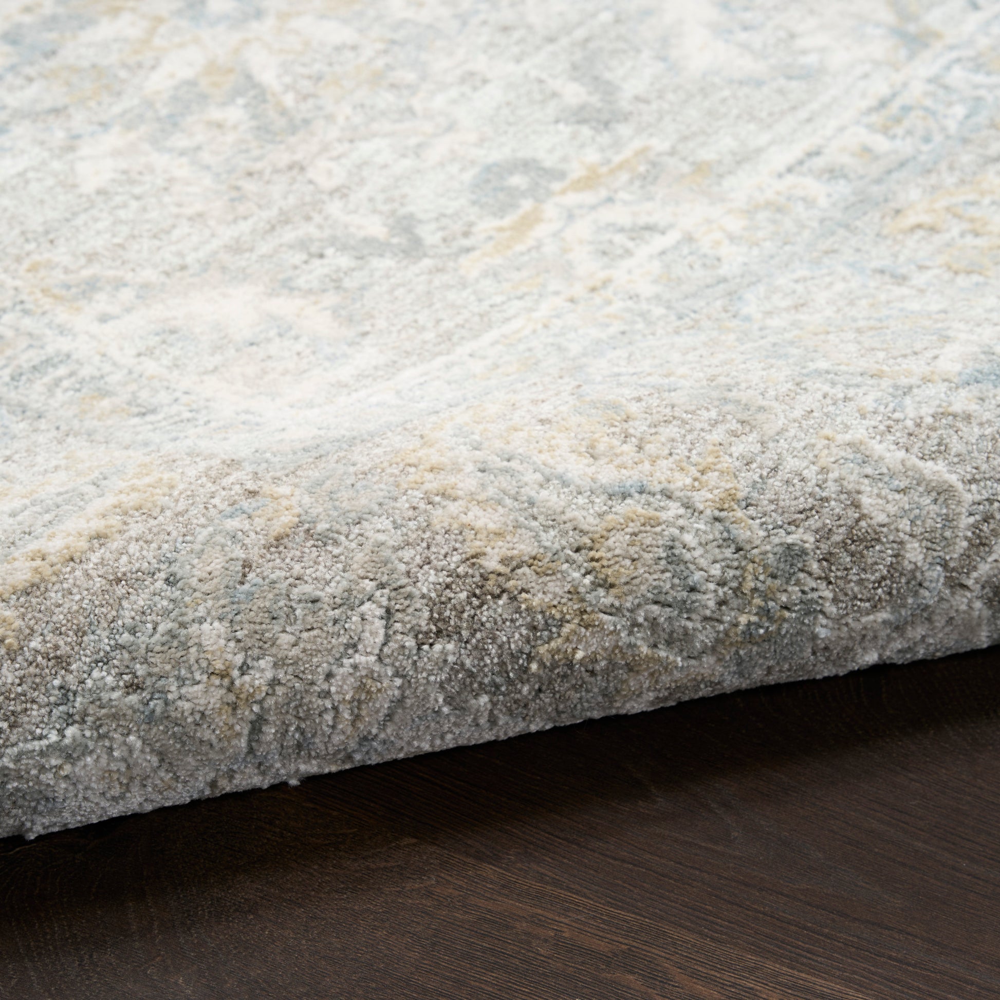 Soft gray-blue rug with subtle ivory abstract pattern and plush texture on dark wood floor.