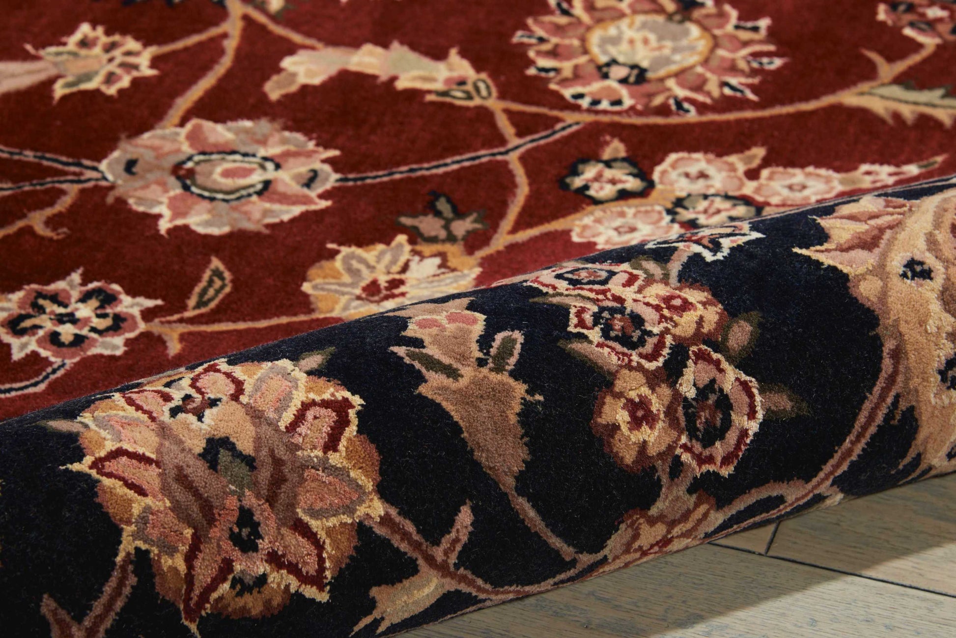 Rolled ornate oriental rug with burgundy field and cream, gold, and blue floral motifs along a dark border.