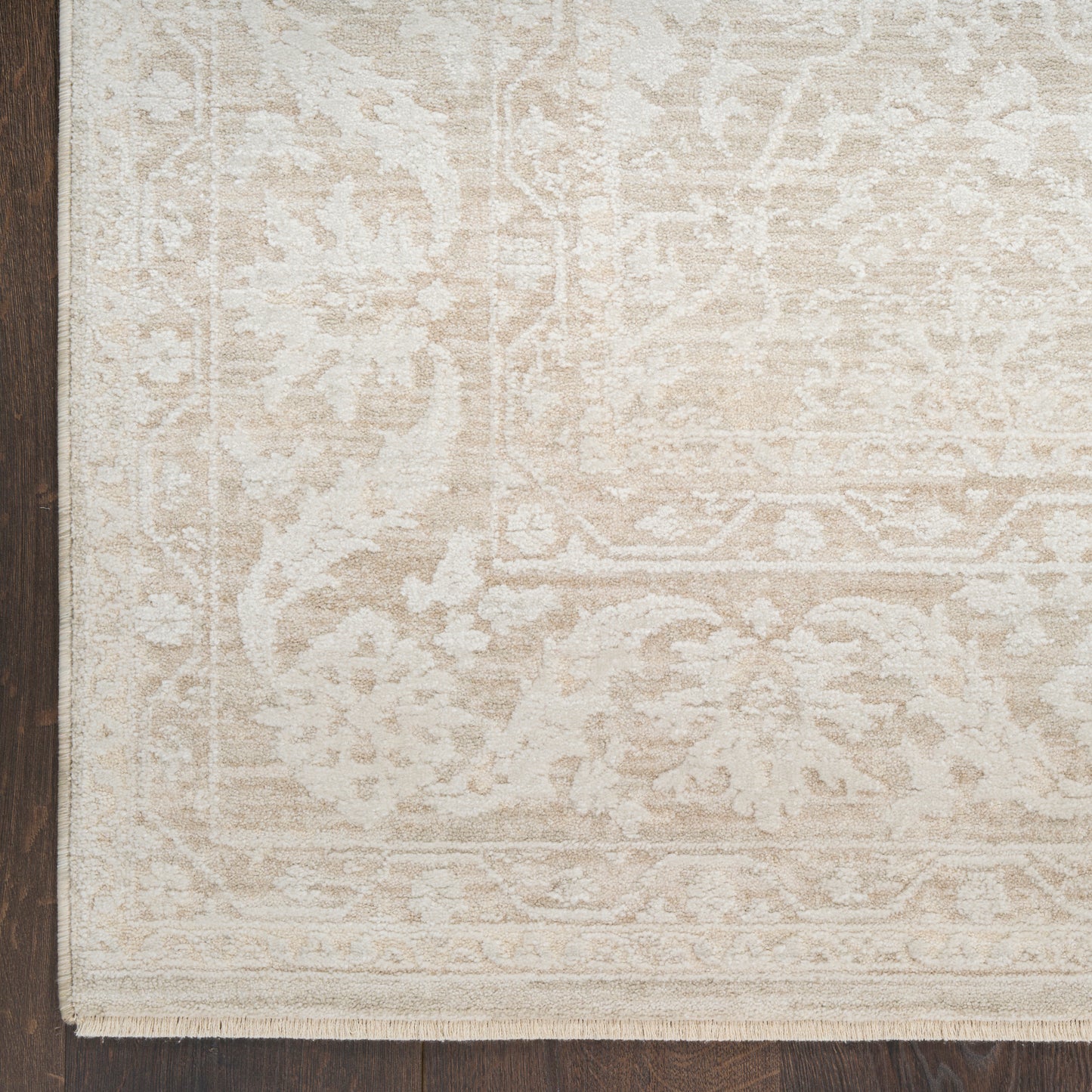 Rectangular cream-beige oriental-pattern area rug with fringe on dark wooden floor.