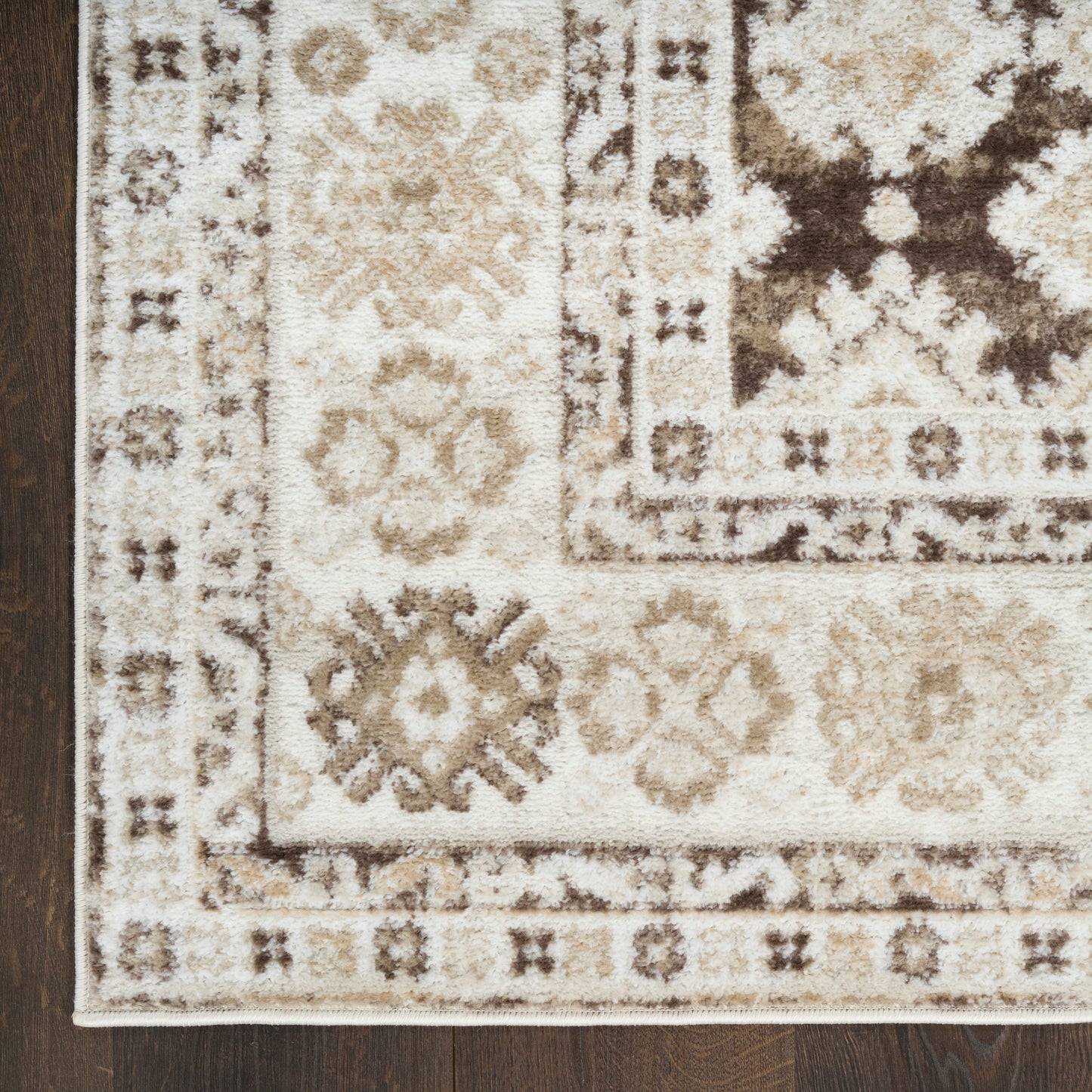 Cream & tan oriental rug with brown geometric floral motifs & bordered edges, partially on dark wood floor.
