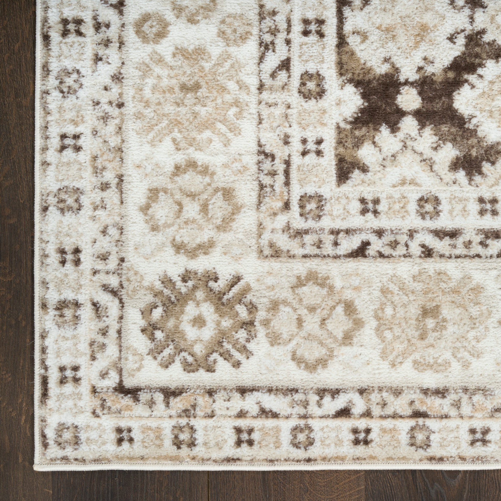 Cream & tan oriental rug with brown geometric floral motifs & bordered edges, partially on dark wood floor.