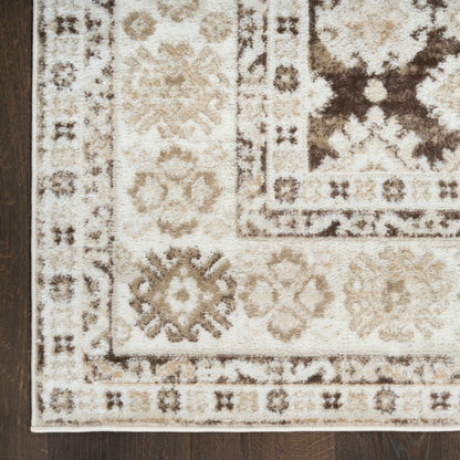 Cream & tan oriental rug with brown geometric floral motifs & bordered edges, partially on dark wood floor.