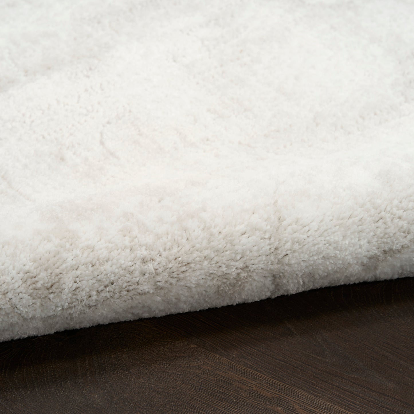 White plush shag rug with a soft high-pile texture resting on a dark wooden floor